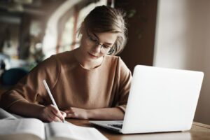 mujer trabajadora enfocada gafas moda concentrandose escribir ensayos sentada acogedor cafe cerca computadora portatil trabajando tomando notas cuidado 197531 21320