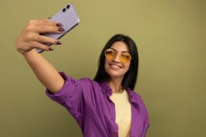 smiling pretty brunette woman sun glasses holds looks phone taking selfie isolated olive green wall 141793 66137